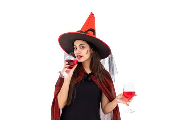 femme asiatique utilisant le costume d’halloween comme sorcière dans le manteau rouge, sur le fond blanc, retenant le verre et buvant le vin rouge, regardant l’appareil-photo - witch beauty beautiful women photos et images de collection