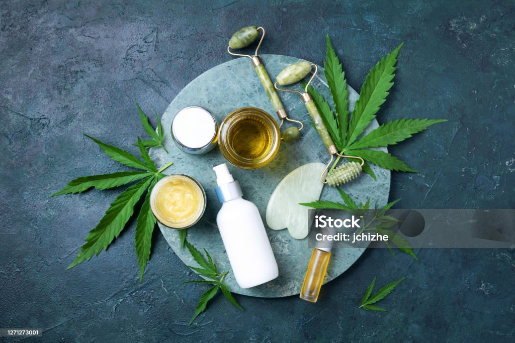 Hemp leaves, oil, cosmetic products, face cream, body butter, face roller and gua sha massager on dark background. Top view, copy space. Natural skin and self care concept. Flat lay. Banner. Hemp leaves, oil, cosmetic products, face cream, body butter, face roller and gua sha massager on dark background. Top view, copy space. Natural skin and self care concept. Flat lay. Banner Cannabidiol Stock Photo