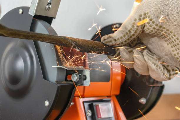 istock Master sharpens on the machine metal knife lawn mower. The master's hand in white gloves holding metal plate 1271274131