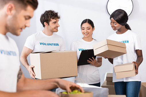 Selective focus of multiethnic volunteers holding clipboard and boxes in charity center