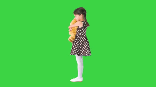 Little girl in polka dot dress hugging teddy bear really tight smiling at camera on a Green Screen, Chroma Key