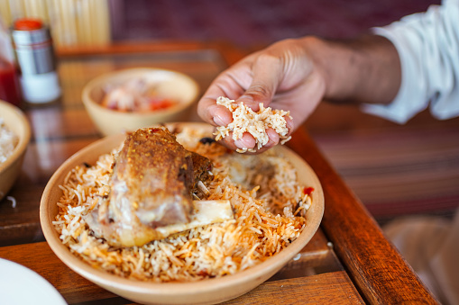 Man eating using hand a traditional biryani rice and chicken dish in local restaurant, Oman