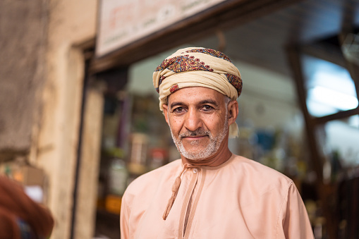 Nizwa / Oman - February 15, 2020: Portrait of adult Muslim Omani man shop seller wearing traditional clothing in Nizwa covered souq