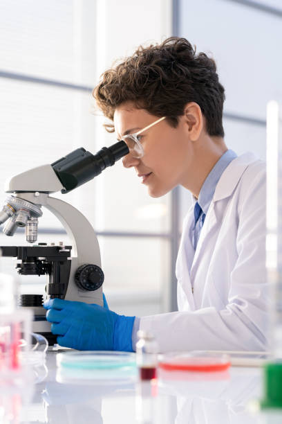 istock Young woman in whitecoat and gloves working with microscope in laboratory 1271279514