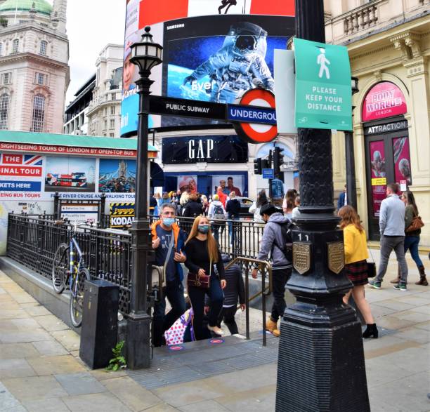 People with protective face masks at Piccadilly Circus, London London, United Kingdom - August 29 2020: People with protective face masks exit Piccadilly Circus Underground Station soho billboard stock pictures, royalty-free photos & images