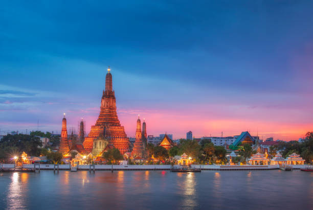 освещенный храм ват арун на реке чао прайя на закате в бангкоке, таиланд - bangkok traditional culture river nautical vessel стоковые фото и изображения