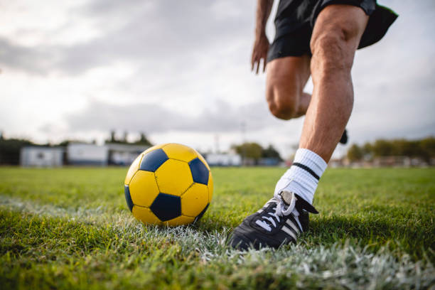 Low Angle Action Portrait of Footballer Running to Kick Ball Surface level close-up of strong male athlete in early 40s approaching ball for kick on sports field. kicking stock pictures, royalty-free photos & images