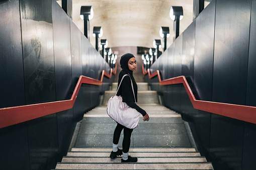 high angle view on young muslim sports woman with sports hijab standing on concrete stairs of subway
station in Berlin and looking back to camera