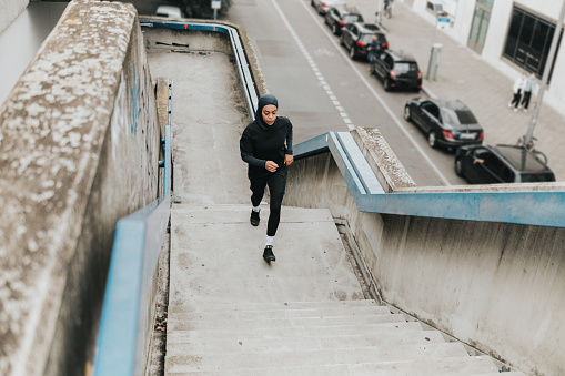 high angle view on young muslim sports woman with sports hijab running up concrete stairs  in Berlin