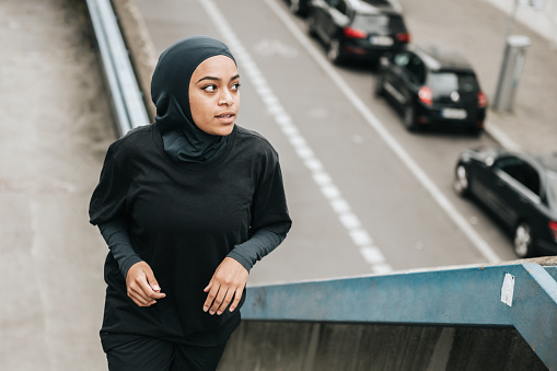 high angle view on young muslim sports woman with sports hijab running up concrete stairs  in Berlin