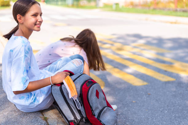 istock Two schoolgirls sitting on the sidewalk while waiting for a bus 1271285691