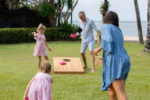 晴れた夏の日に海のそばでコーンホールゲームをする幸せな家族。親子がビーンバッグのスツを演奏 - cornhole leisure games outdoors color image ストックフォトと画像