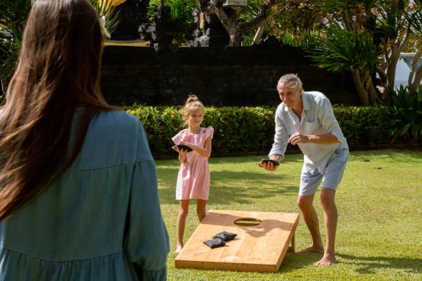 晴れた夏の日に屋外でコーンホールゲームをプレイハッピーファミリー。親子がビーンバッグのスツを演奏 - cornhole leisure games outdoors color image ストックフォトと画像
