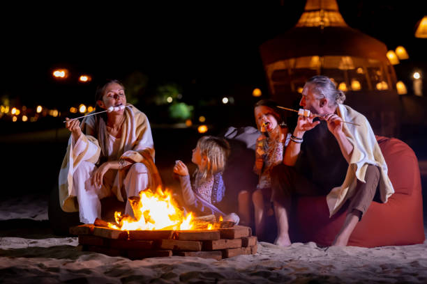 Happy family camping on beach sitting around bonfire and toasting marshmallows Happy family camping on beach sitting around bonfire and toasting marshmallows. Summer vacation family bbq beach stock pictures, royalty-free photos & images