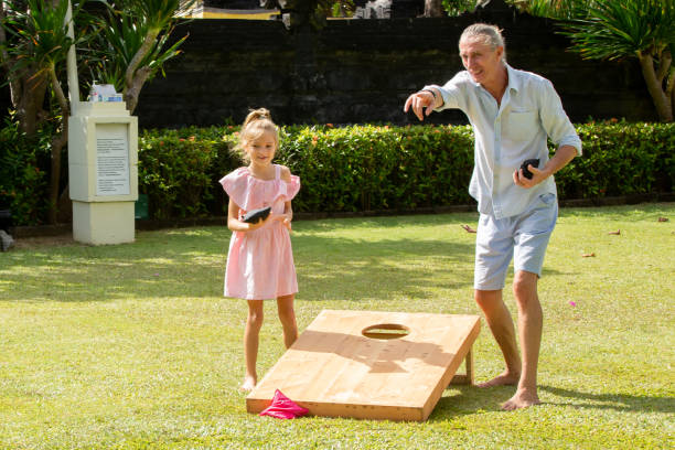 szczęśliwa rodzina gra w cornhole gry na świeżym powietrzu w słoneczny letni dzień. rodzice i dzieci grające w torebce z fasoli toss - cornhole leisure games outdoors color image zdjęcia i obrazy z banku zdjęć
