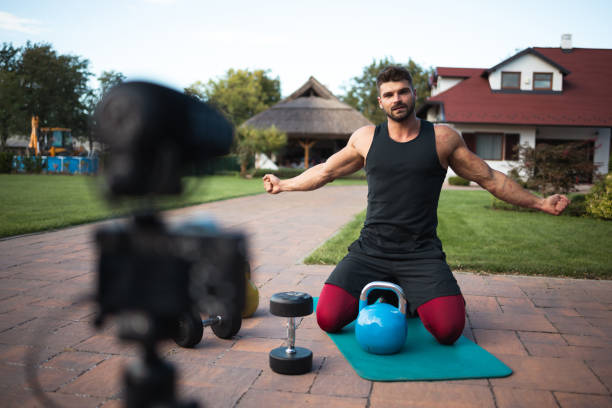 istock Male athlete sitting on exercise mat and making vlog at backyard. 1271295187