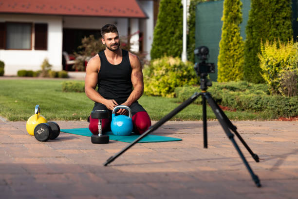 istock Male athlete sitting on exercise mat and making vlog at backyard. 1271295382