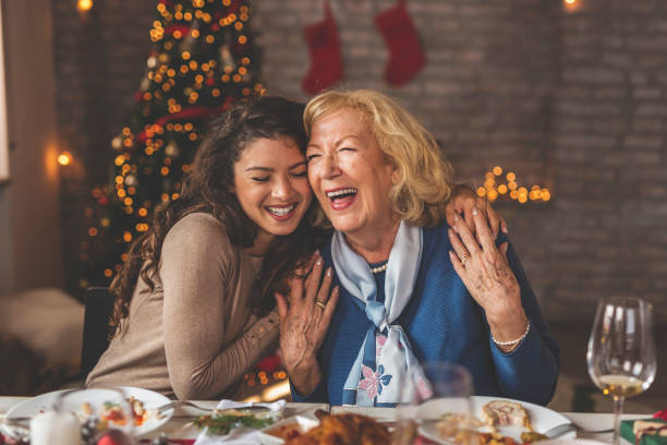 Mother and daughter hugging over Christmas dinner Family having Christmas dinner at home, gathered around the table, enjoying their time together; daughter hugging her mother and smiling dinner stock pictures, royalty-free photos & images