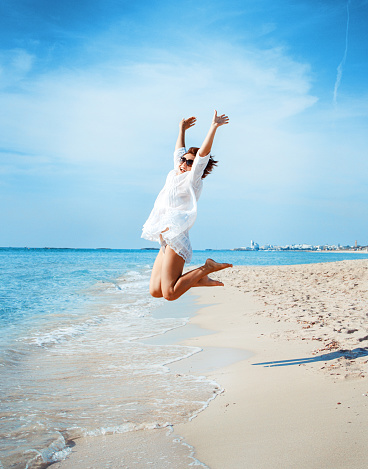 Young woman in white cover up  jump on the beach.  Travel and vacations concept.