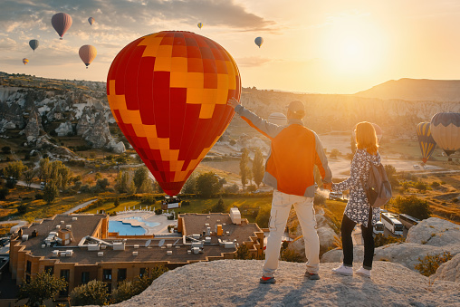 Couple travelers watches colorful balloons flying on an early sunny morning in Goreme Valley, Cappadocia. Turkey. Cappadocia one of the best places to fly with hot air balloons.