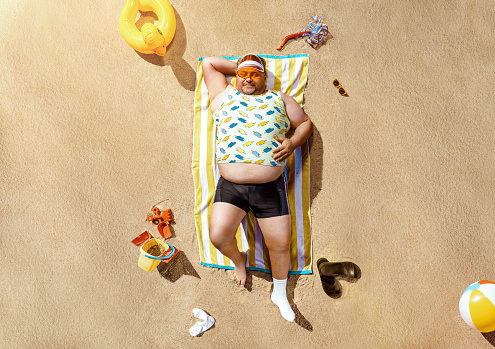 High angle view of funny overweight tourist resting on the beach with copy space