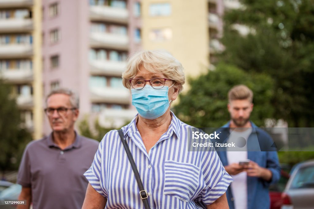 Senior woman wearing face mask Outdoor portrait of senior woman wearing a N95 face mask standing in front of block of flats in the city. 65-69 Years Stock Photo