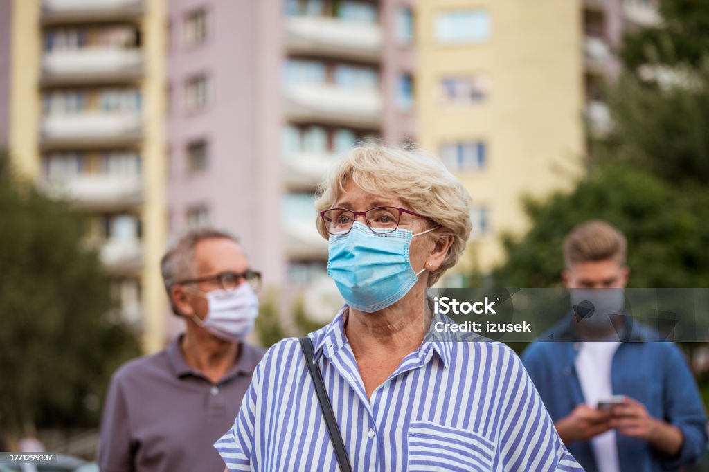Senior woman wearing face mask Outdoor portrait of senior woman wearing a N95 face mask standing in front of block of flats in the city. Defocused Stock Photo