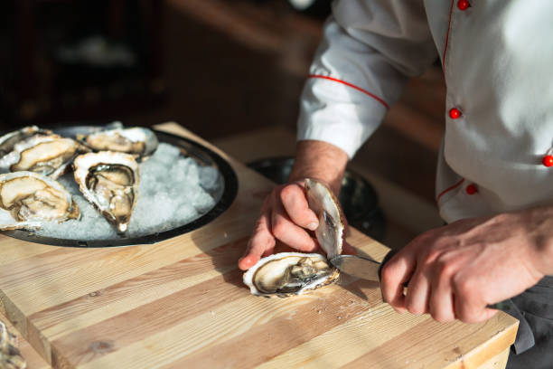 öffnen der hohlen und flachen austern. chef öffnet austern im restaurant. - schälen essen zubereiten stock-fotos und bilder