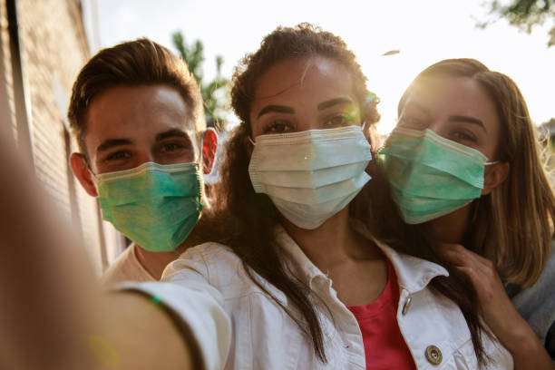 istock Three young people in protective face masks taking selfies 1271302326