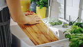 Close Up Shot of a Person Washing a Chopping Board with a Cleaning Liquid Under Tap Water. Using Dishwasher in a Modern Kitchen. Natural Clean Home and Healthy Way of Life Concept.