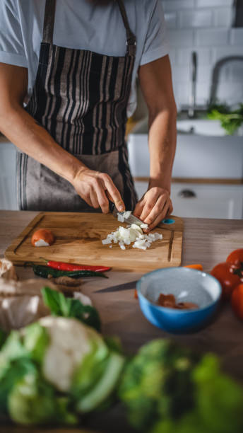 istock Handsome Man Chopping a Green Spring Onion with a Sharp Kitchen Knife. Man in White Shirt and Apron is Making a Organic Salad Meal in a Modern Sunny Kitchen. Natural Clean Diet and Healthy Lifestyle. 1271304070