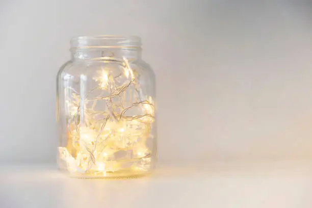 Photo of Yellow christmas lights in a glass jar on a white background