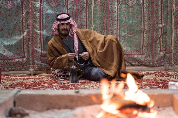 istock Bedouin man wearing traditional clothes praying with a tasbih while drinking tea on a carpet in front of a fire in the Saudi desert 1271307952
