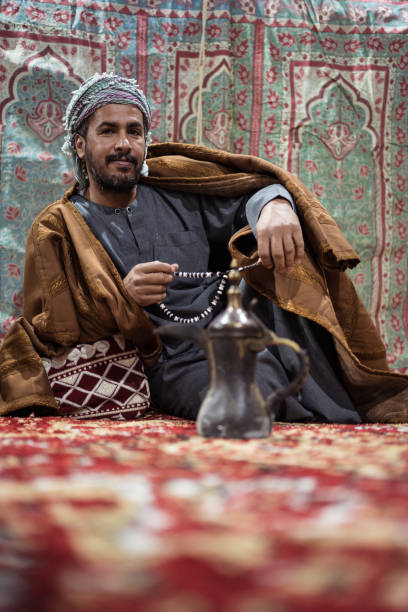 istock Bedouin man wearing traditional clothes praying with a tasbih while drinking tea on a carpet in the Saudi desert 1271308017
