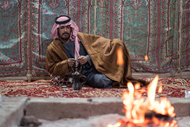 istock Bedouin man wearing traditional clothes praying with a tasbih while drinking tea on a carpet in front of a fire in the Saudi desert 1271308023