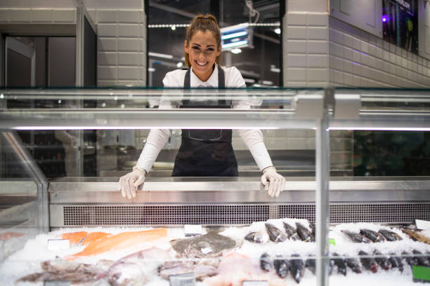 Portrait of supermarket deli worker working in fish department. Frozen fish on the ice ready for sale. Portrait of supermarket deli worker working in fish department. Frozen fish on the ice ready for sale. fish market photos stock pictures, royalty-free photos & images