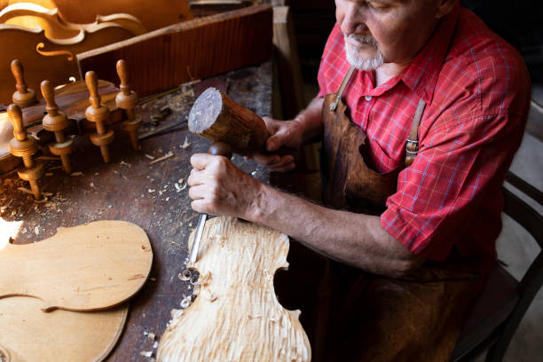 istock An experienced, gray haired senior man carpenter working on his project in carpentry workshop. Man using hummer and knife for carving wood plank. 1271311179