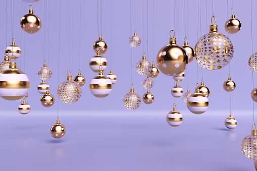 Glass gold and white christmas balls suspended on thin threads on a light purple background