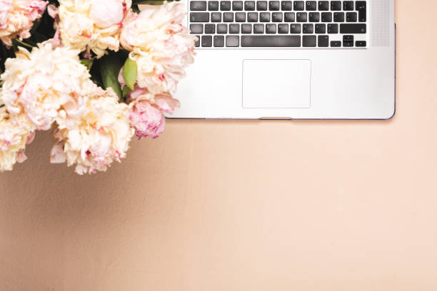 Workspace with keyboard laptop and peony flowers. Top view on a pink desk, flat lay with copy space. Office business concept