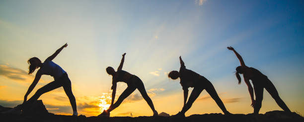 Silhouette of young womans practicing yoga or pilates at sunset or sunrise in beautiful mountain location. Silhouette of young womans practicing yoga or pilates at sunset or sunrise in beautiful mountain location group sunrise yoga stock pictures, royalty-free photos & images