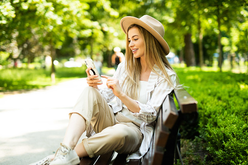 Young blonde woman using phone in city park.