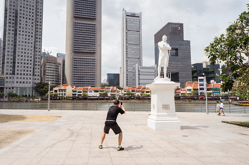 Singapore City / Singapore - February 15, 2019: Asian tourist taking photo of sculpture in weird position in the city of Singapore