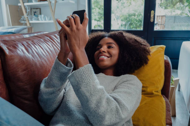 istock Pretty mixed race female smiling while scrolling on smartphone resting on leather sofa in trendy lounge 1271319525