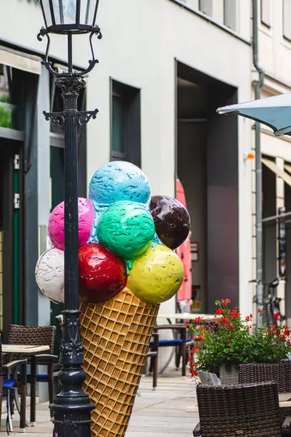 Colorful model of an ice cream cone outside a shop or ice-cream parlour attached to an old wrought iron lamppost at an outdoor restaurant