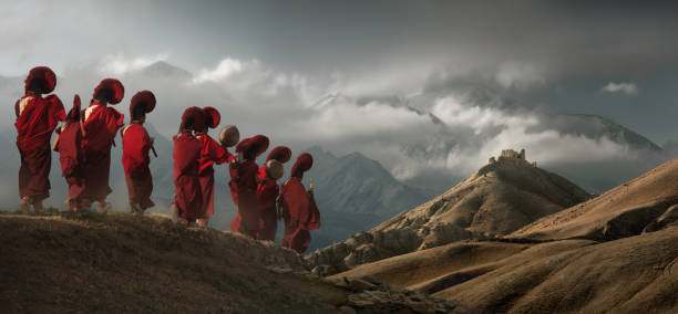 junge mönche in traditioneller kleidung laufen vor dem hintergrund der berge zu einem alten tempel im königreich mustang, nepal. - tibetan buddhism stock-fotos und bilder