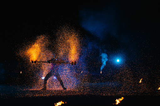 Espectáculo de fuego, bailando con llamas, maestro masculino haciendo malabares con fuegos artificiales, actuación al aire libre, dibuja una figura ardiente en la oscuridad, chispas brillantes en la noche. Un hombre con traje LED baila con fuego. photo