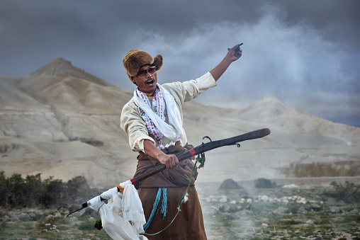 LO-MANTANG, NEPAL - MAY 14, 2018: Tibetan man in national clothes shoots from an old gun at the end of the Tiji festival ceremony in the capital Lo Mantang of the kingdom of Mustang, Nepal.