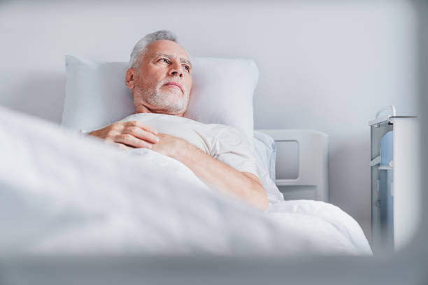 Mature caucasian male patient resting while lying on bed in moderm hospital ward room Mature caucasian male patient resting while lying on bed in moderm hospital ward room hospital depression sadness bed stock pictures, royalty-free photos & images