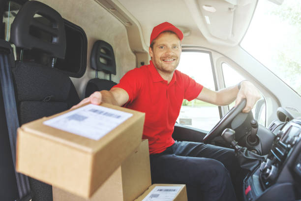 istock young smiling delivery service man sitting in van and delivering boxes. giving package 1271329091