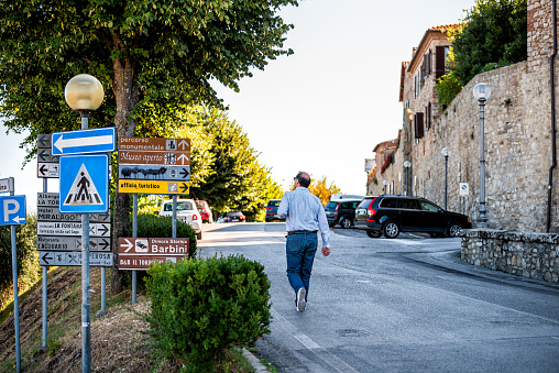 Castiglione del Lago, Italy - August 28, 2018: Umbria sunny summer day with street road and person walking by direction signs exterior of fortress city